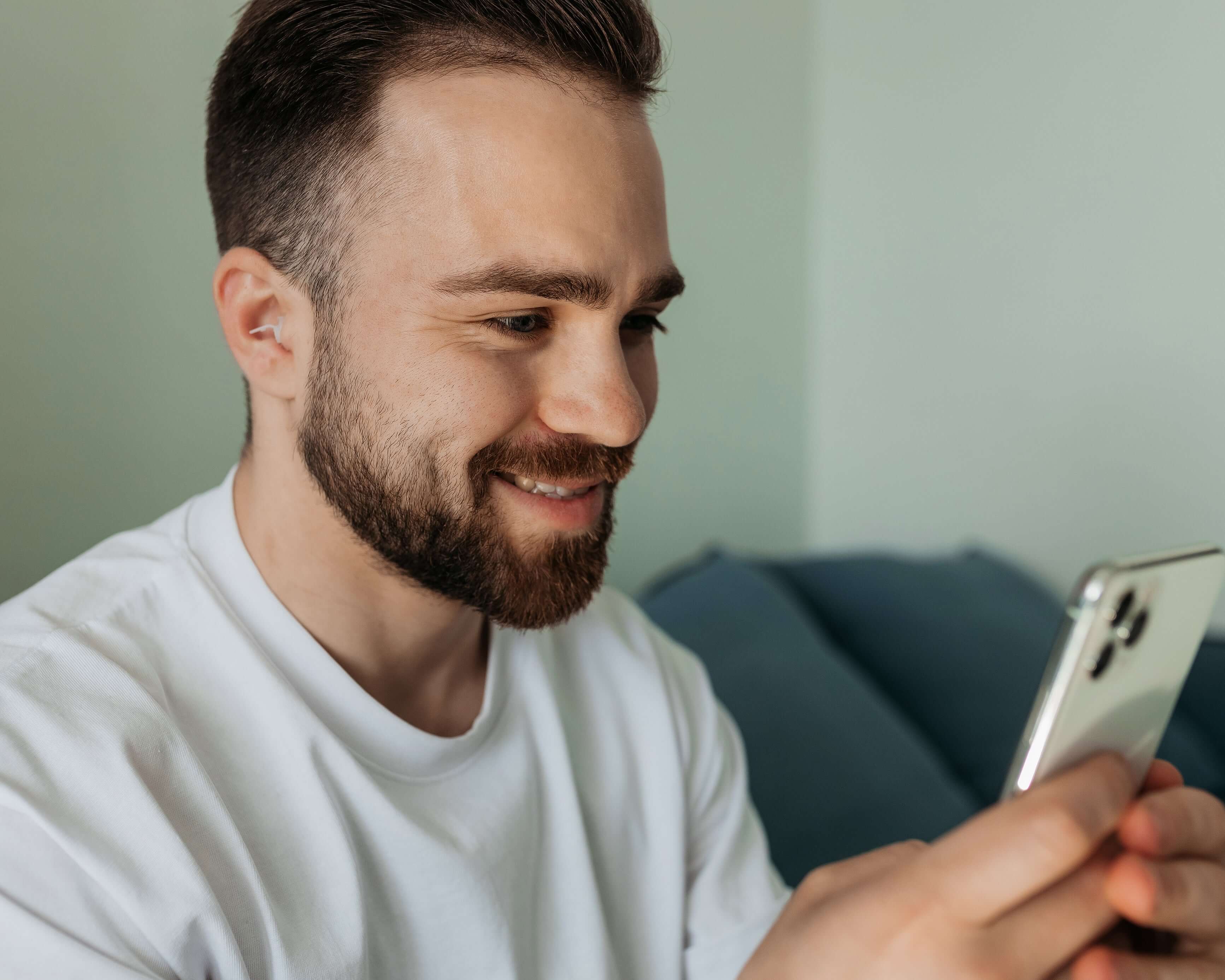 Man wearing Kokon Universe noise reducing earplugs while smiling at his smartphone, illustrating comfort and usability.