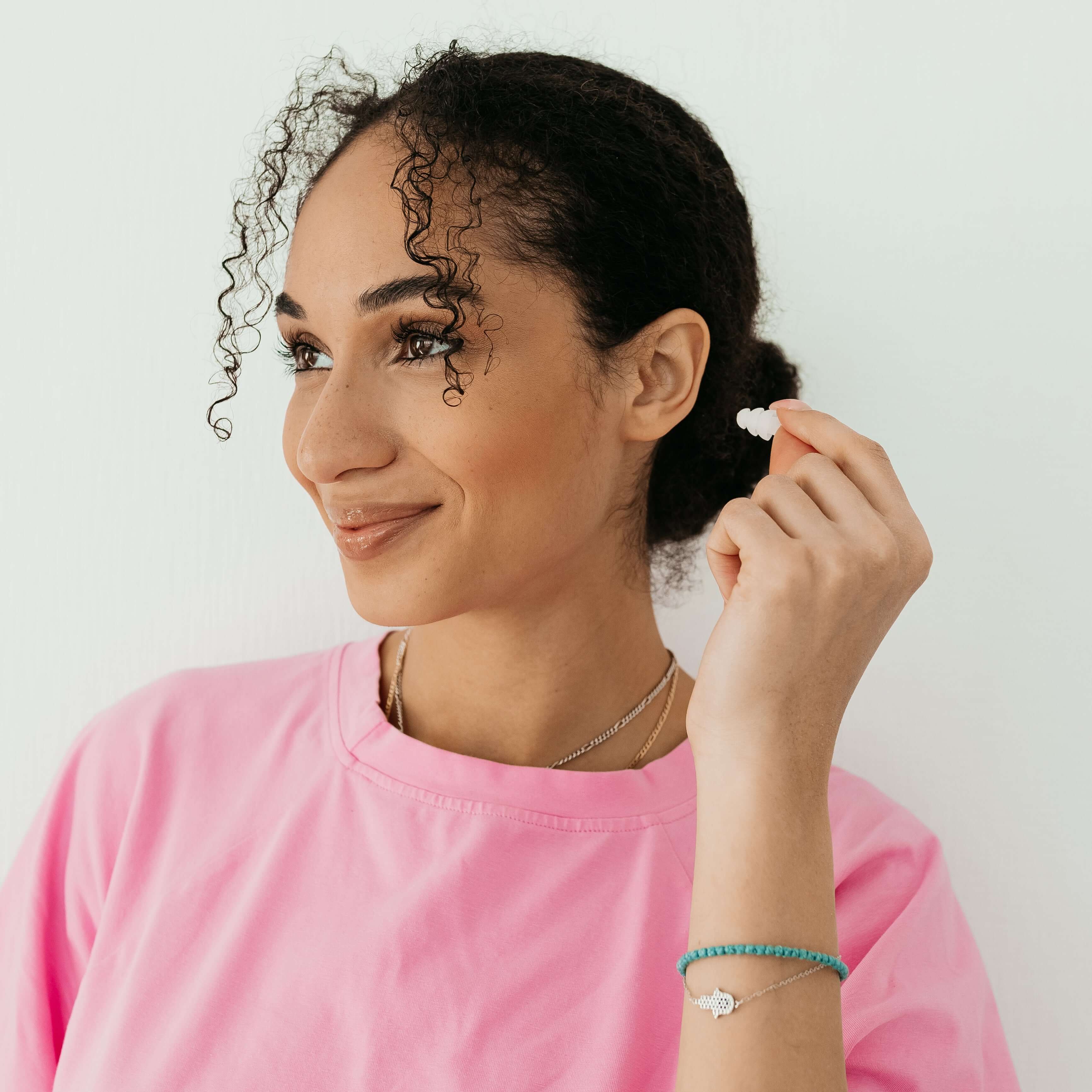 Woman holding Kokon Universe Noise Reducing Sleeping Earplugs in a pink shirt, smiling against a white background.