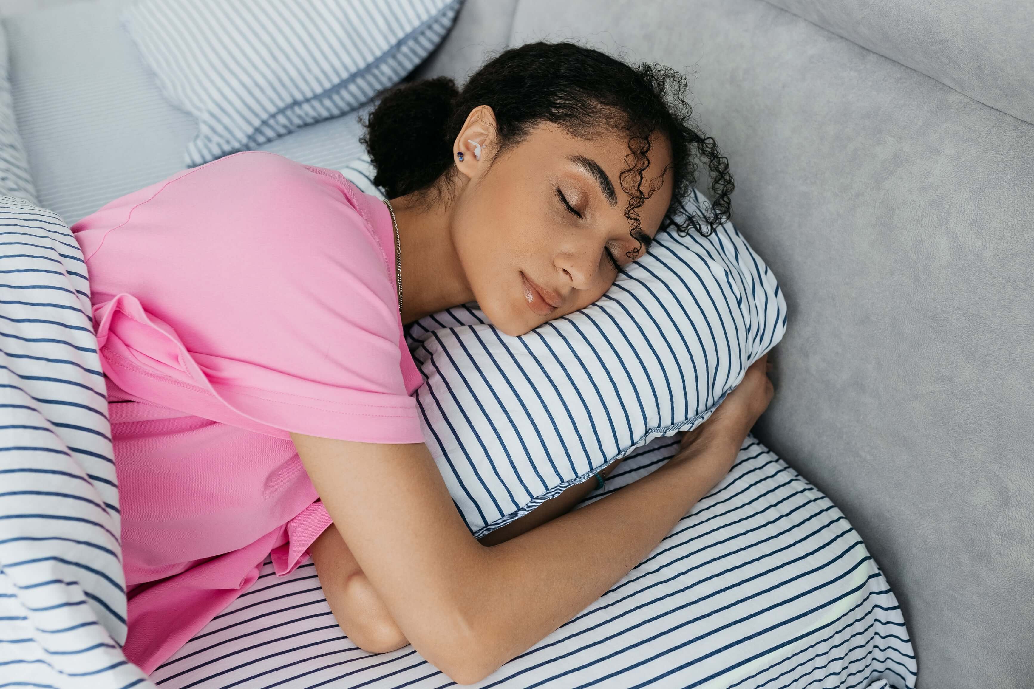 Woman peacefully sleeping on a striped pillow, wearing noise-reducing earplugs for better rest.