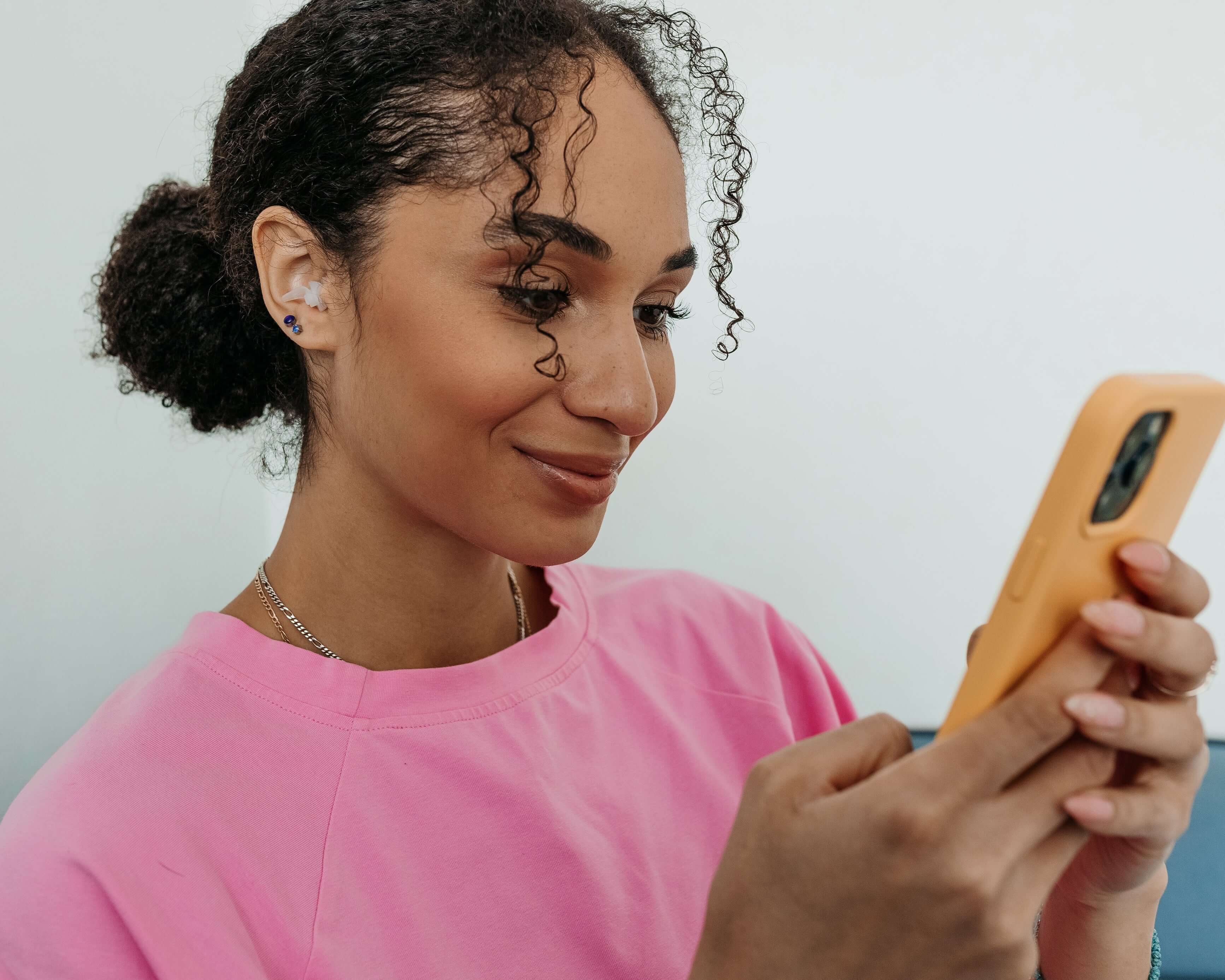 Woman wearing Kokon Universe noise-reducing earplugs while using a smartphone, smiling and enjoying peace.