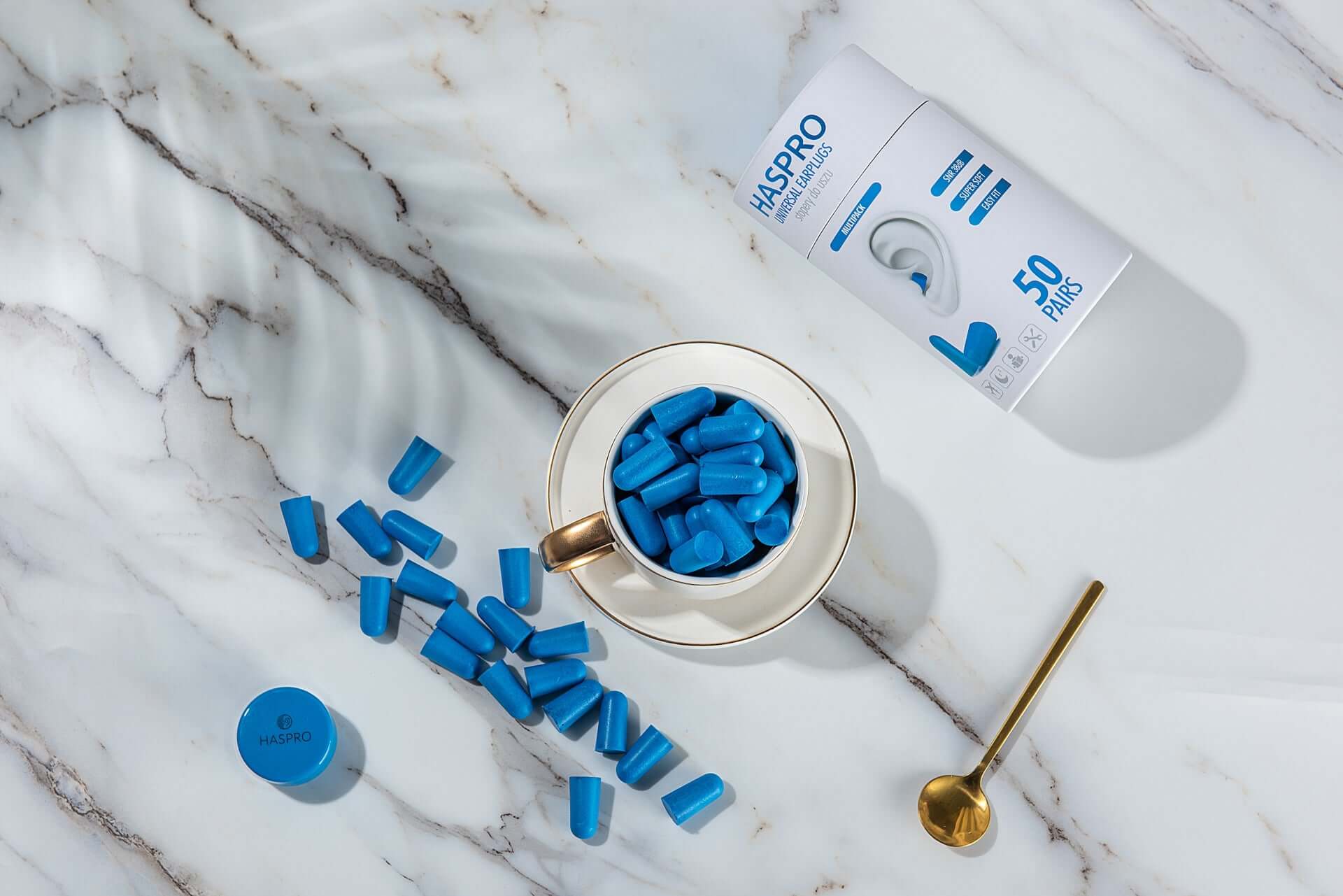 HASPRO foam earplugs in blue color, 50 pairs, displayed in a cup with the packaging on marble surface.