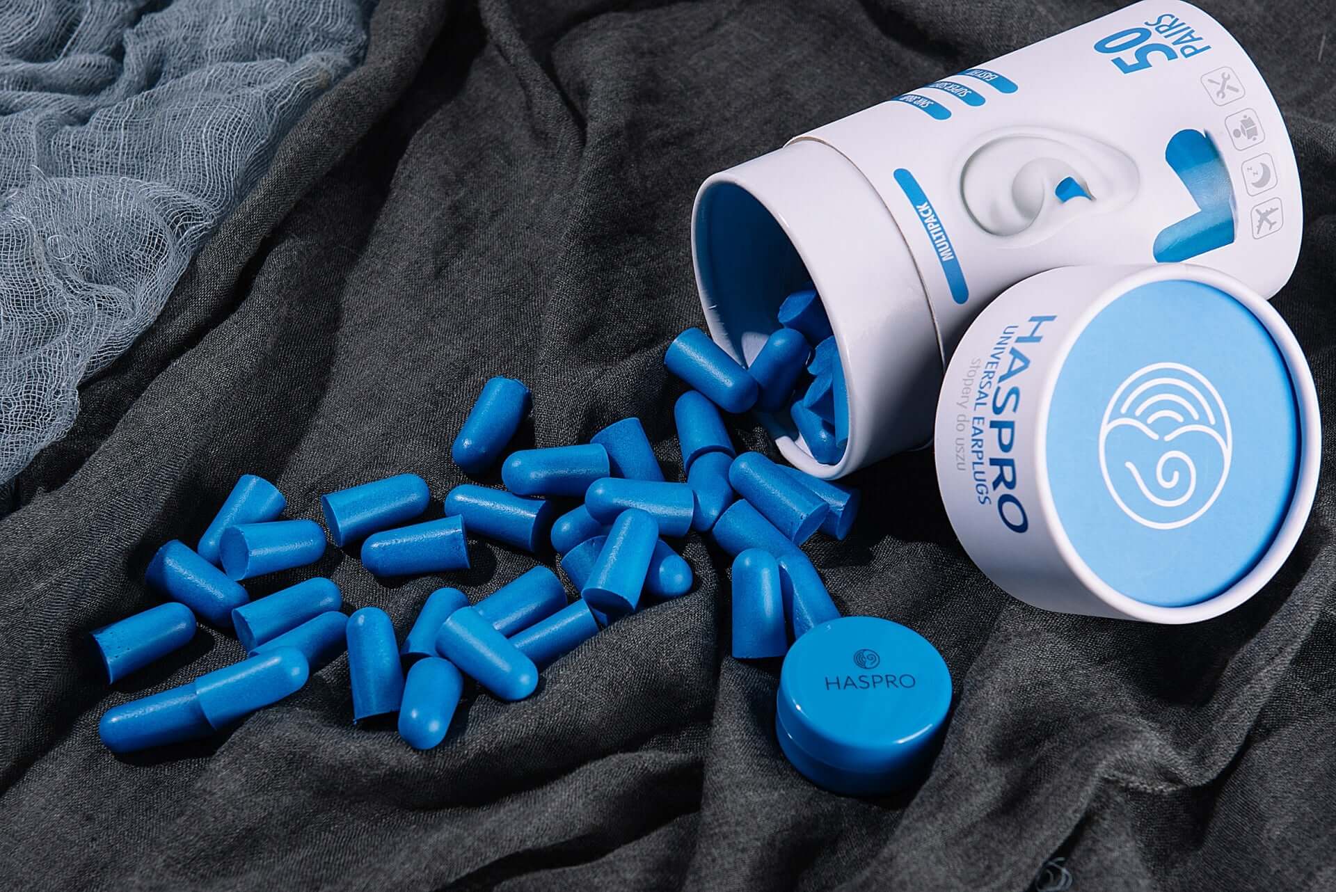 HASPRO Tube50 foam sleeping earplugs in blue scattered next to a plastic case on a dark background.
