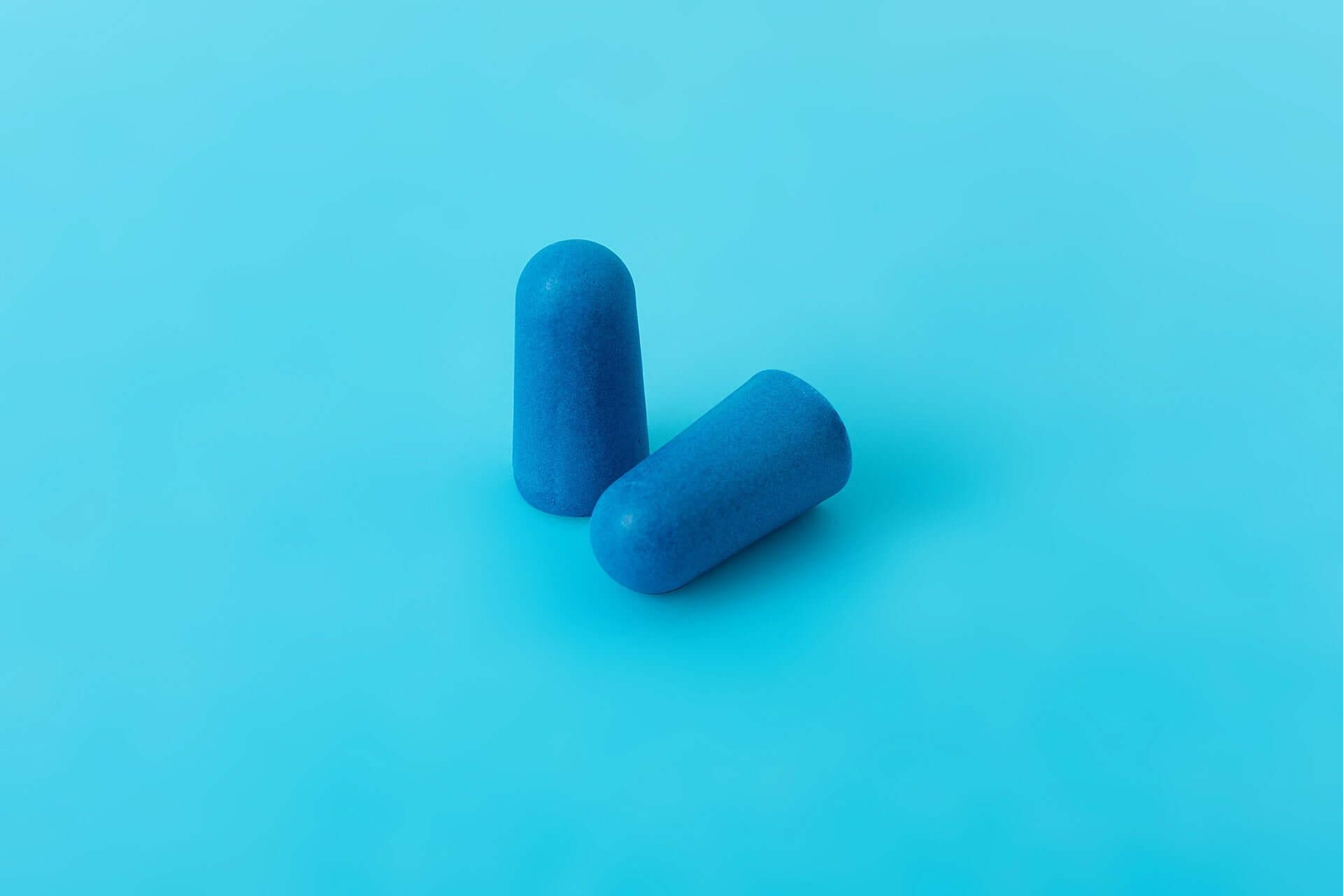 Two blue foam earplugs on a light blue background, designed for high noise reduction and comfort.