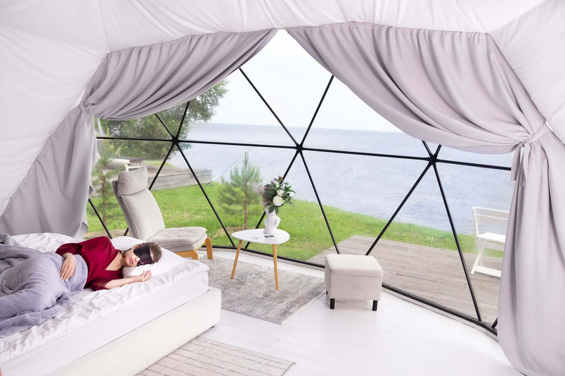 Person sleeping peacefully in a geodesic dome room with a view of nature, wearing a silk sleep mask.