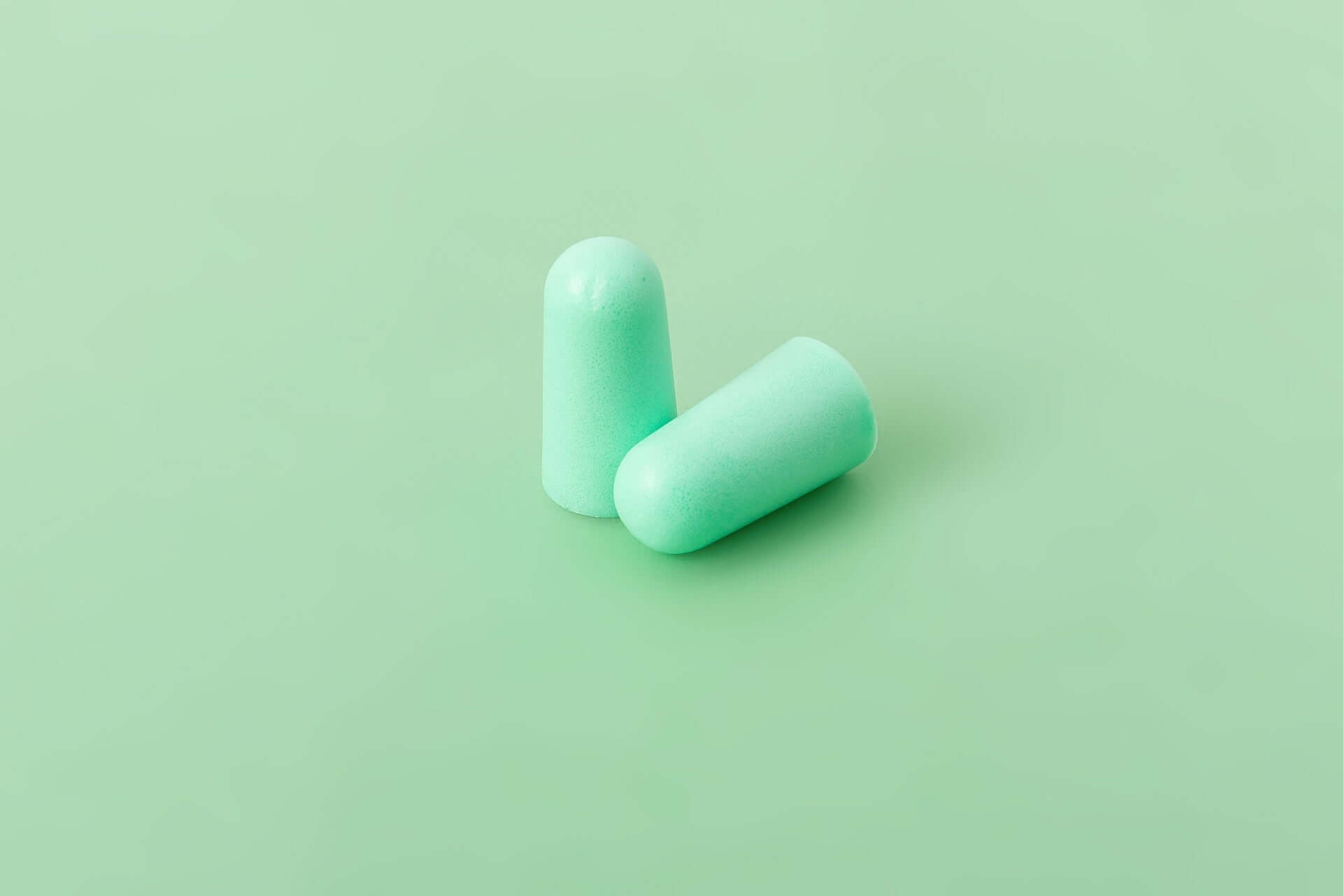 Mint foam sleeping earplugs on a green background, offering high noise reduction of 38 dB for comfortable use.