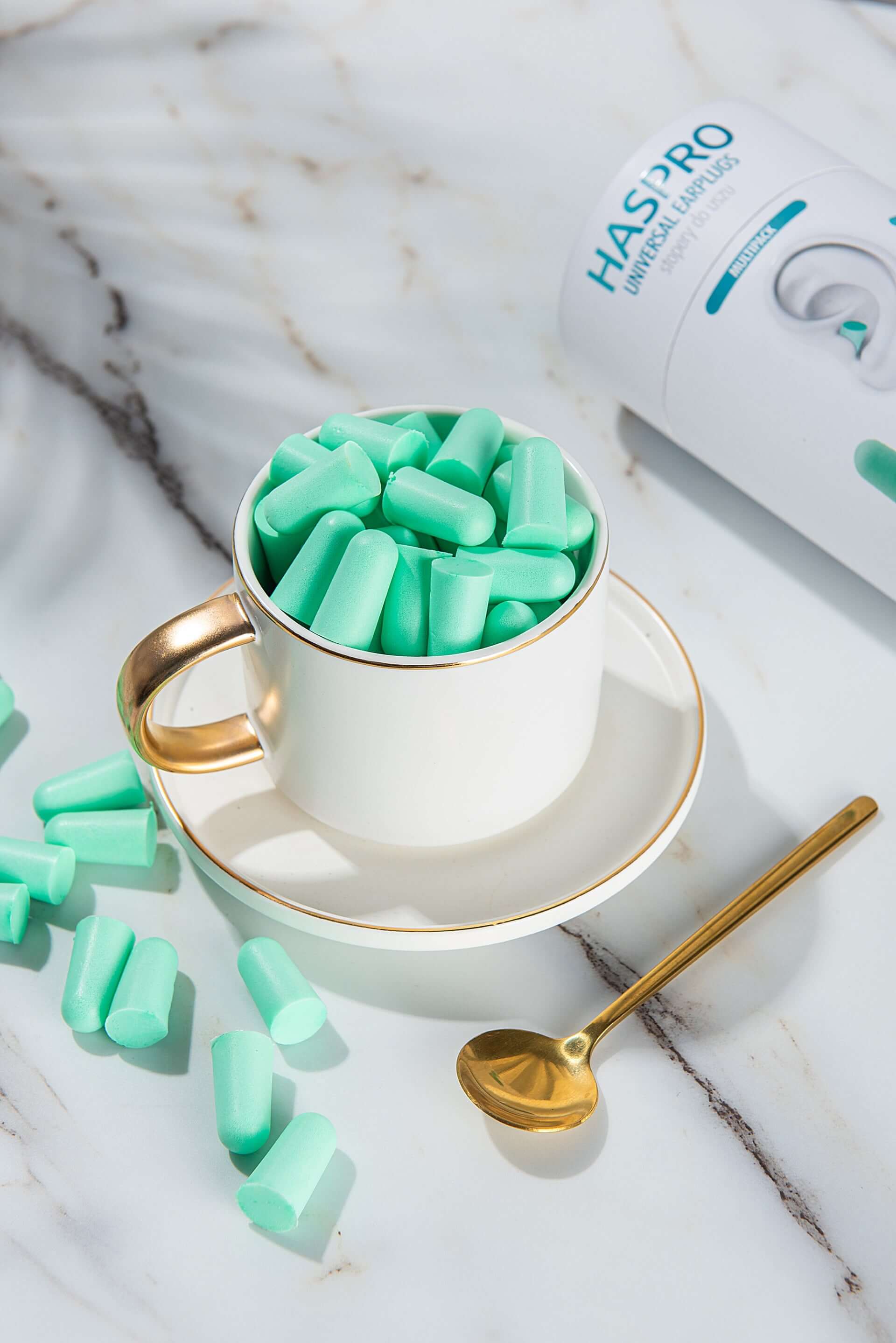 HASPRO foam earplugs in a gold-rimmed cup, showcasing comfort and high noise reduction in mint green.