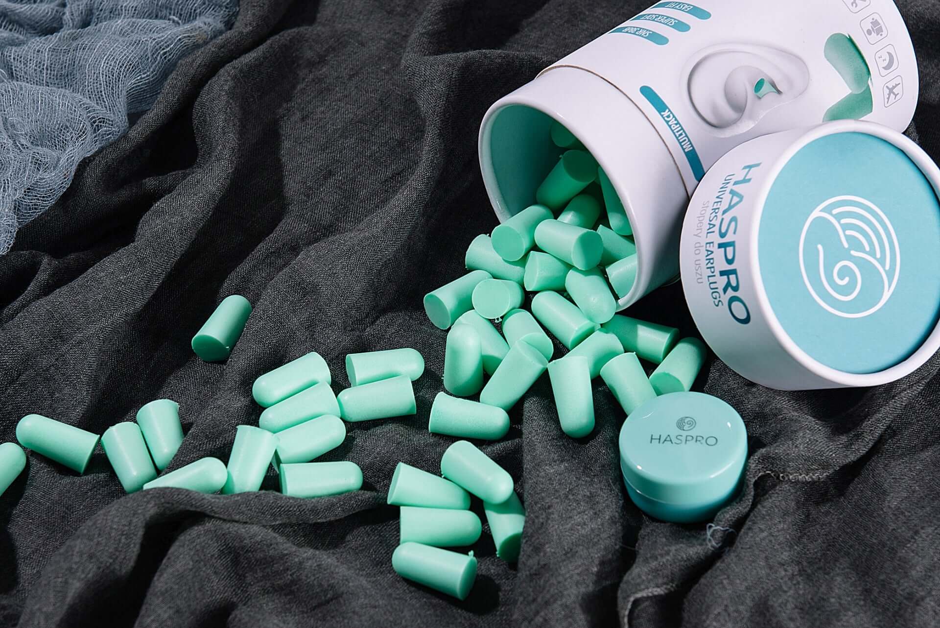 HASPRO Tube50 foam earplugs in mint, spilling from a container on a soft fabric surface, showcasing noise reduction features.