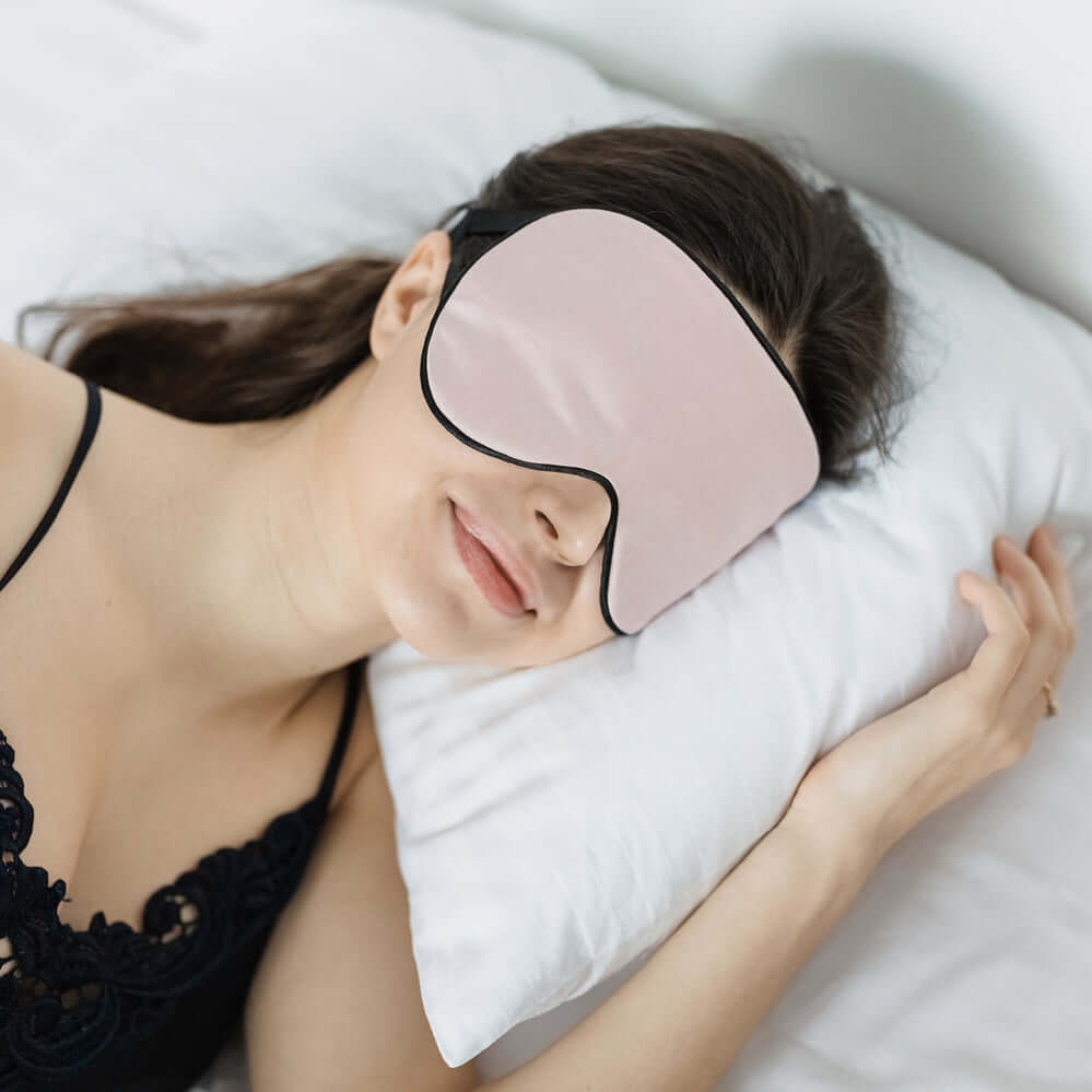 Woman wearing a Quietstore organic cotton sleep mask while resting on a pillow, showcasing comfort and light-blocking features.