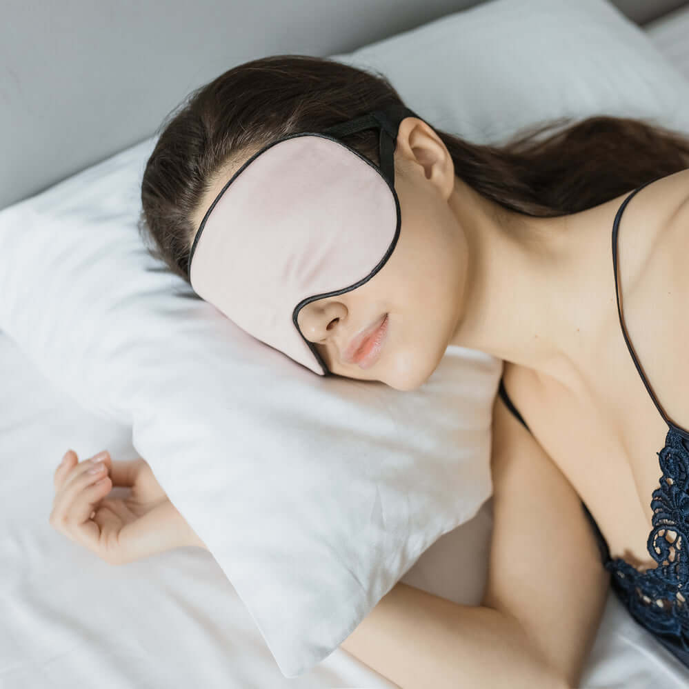 Woman sleeping peacefully with a Quietstore organic cotton sleep mask on white pillows.