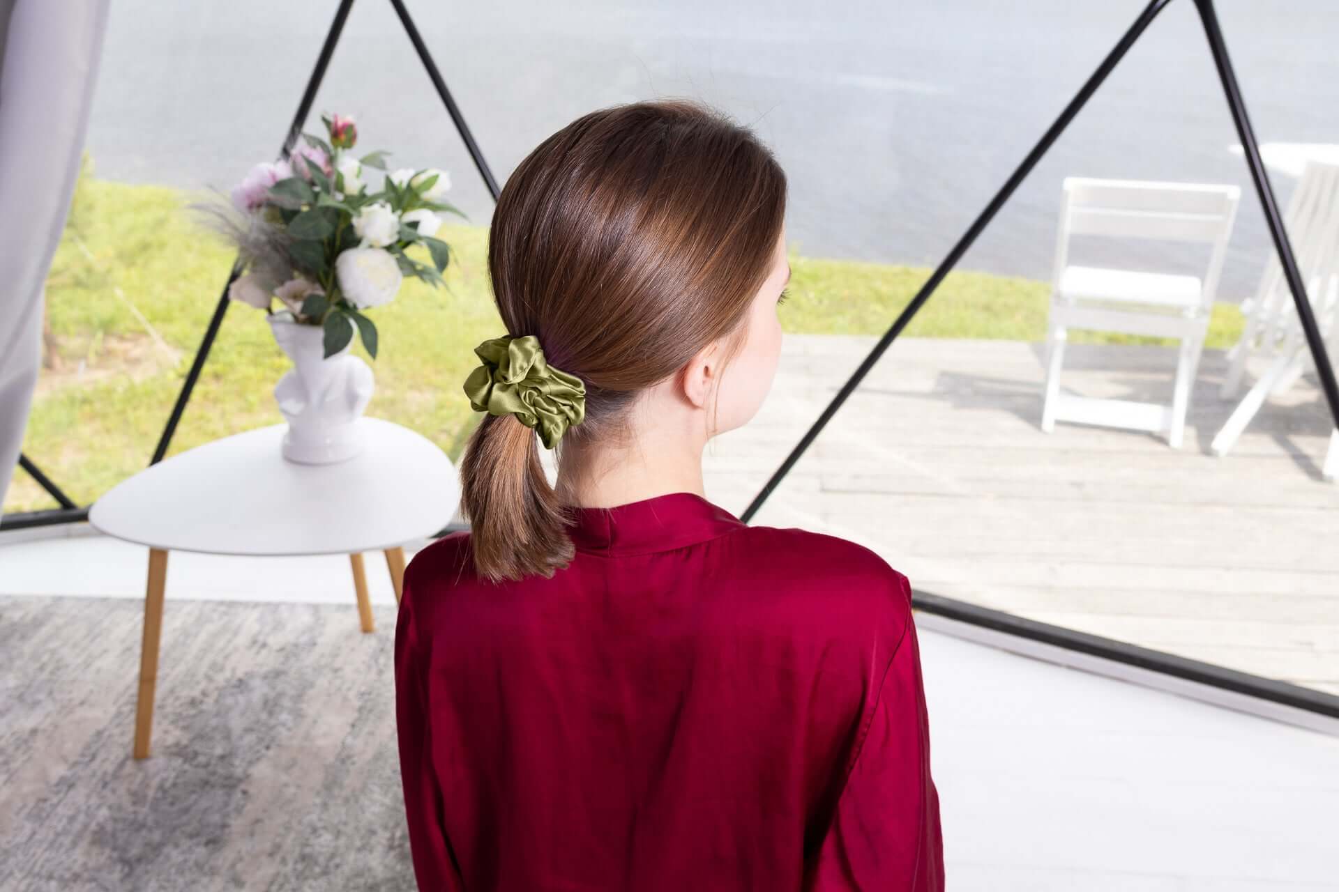 Woman with brown hair wearing a large green mulberry silk scrunchie, showcasing its smooth texture and elegant styling.