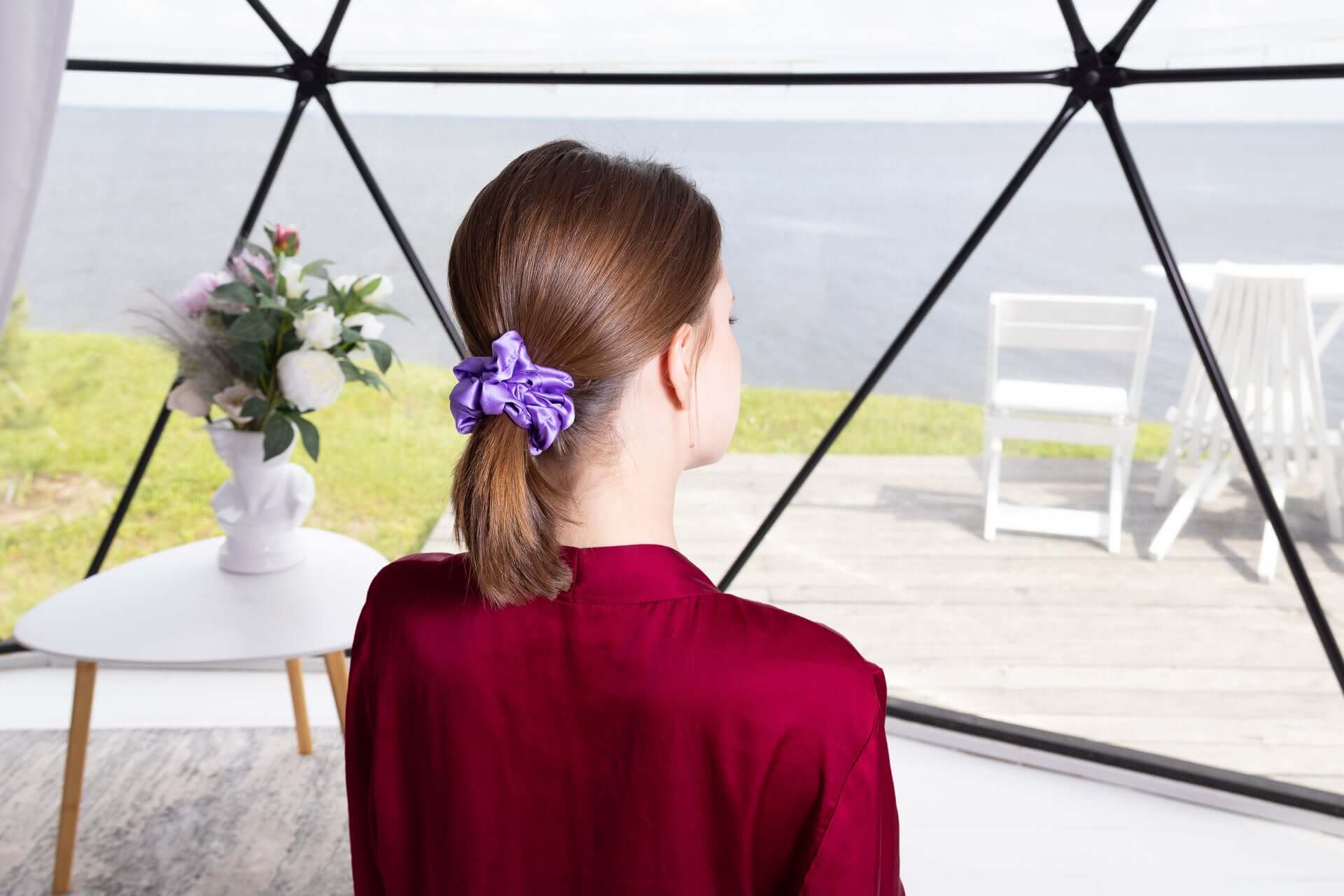 Woman wearing a pure mulberry silk scrunchie in a ponytail, showcasing elegance and comfort in a sleek interior setting.
