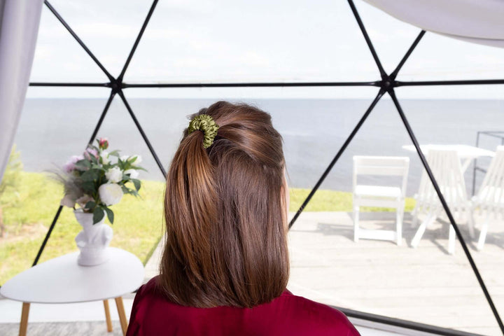 Woman with smooth, brown hair in a ponytail held by a green silk scrunchie by a scenic lake view.