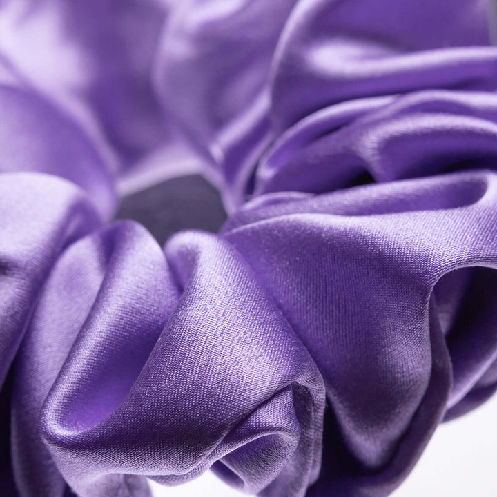 Close-up of a pure mulberry silk scrunchie in vibrant purple, highlighting its smooth texture and durability for hair styling.