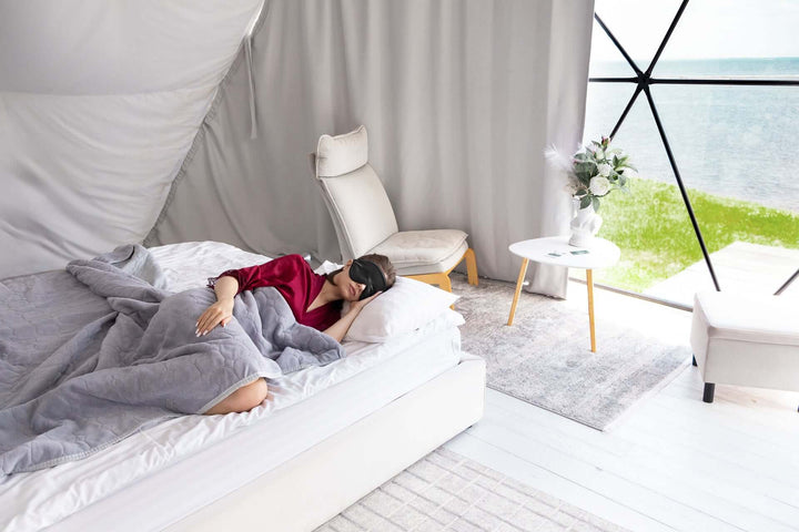 Woman peacefully sleeping in a modern bedroom wearing a silk sleep mask, showcasing relaxation and comfort.