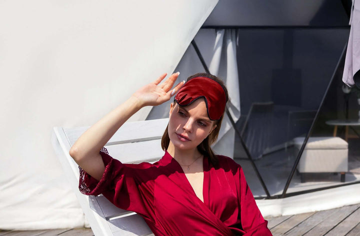 Woman in a red robe wearing a Quietstore 3.0 silk sleep mask, enjoying a relaxing day outdoors.