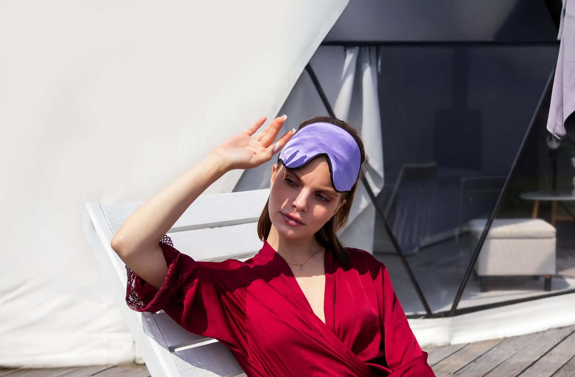 Woman wearing a Quietstore 3.0 silk sleep mask while relaxing outdoors, showcasing soft fabric and stylish design.