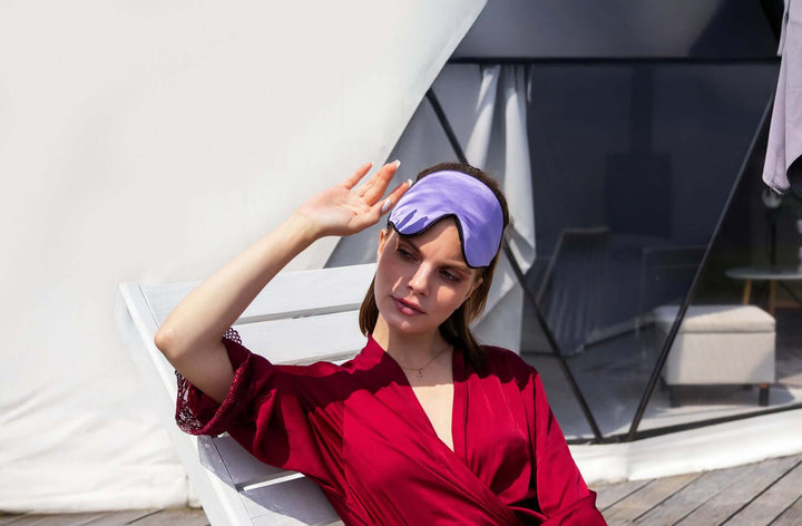 Woman wearing a Quietstore 3.0 silk sleep mask while relaxing outdoors, showcasing soft fabric and stylish design.