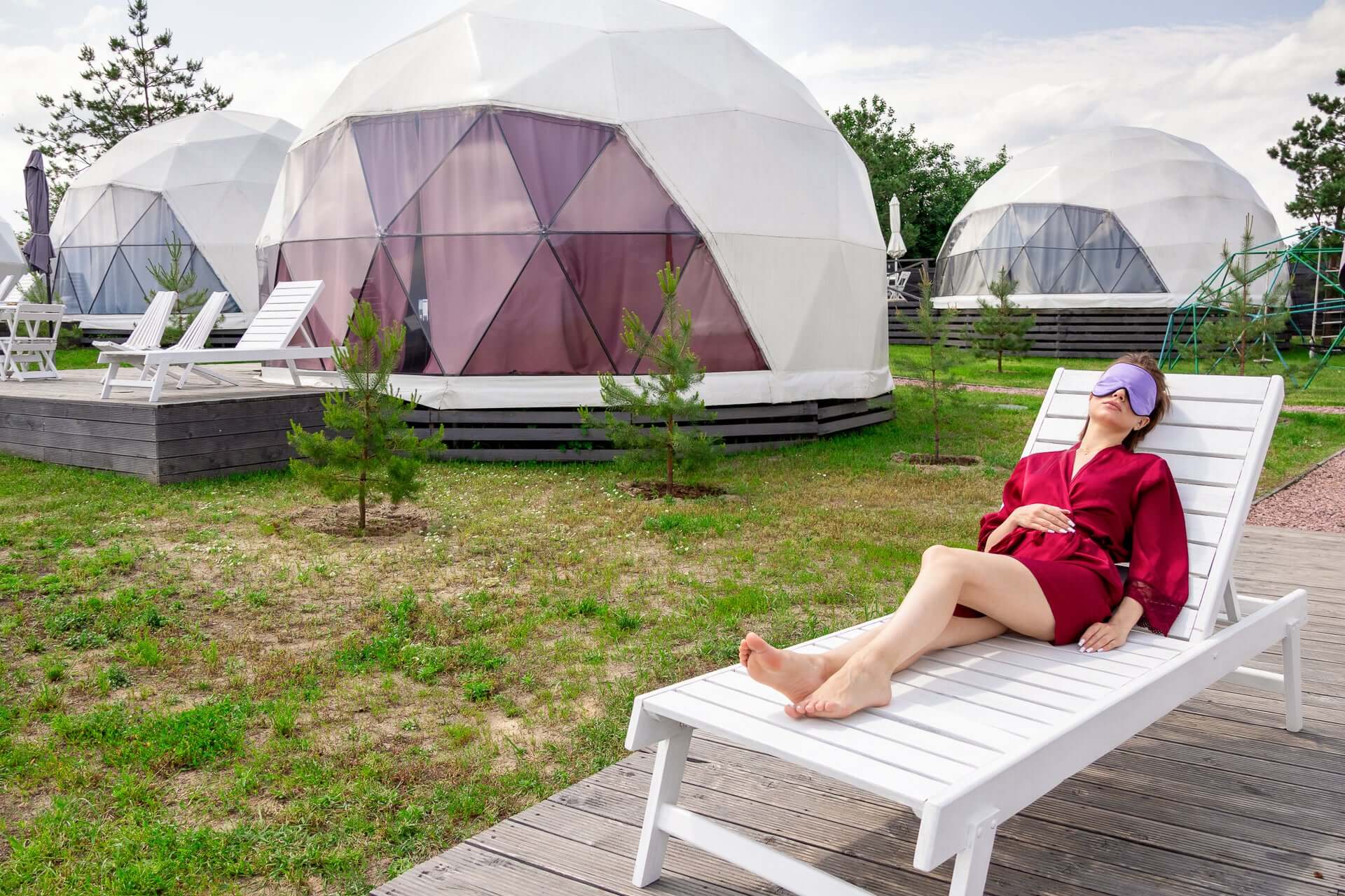 Person relaxing outdoors in a silk sleep mask near geodesic domes, embodying comfort and tranquility.