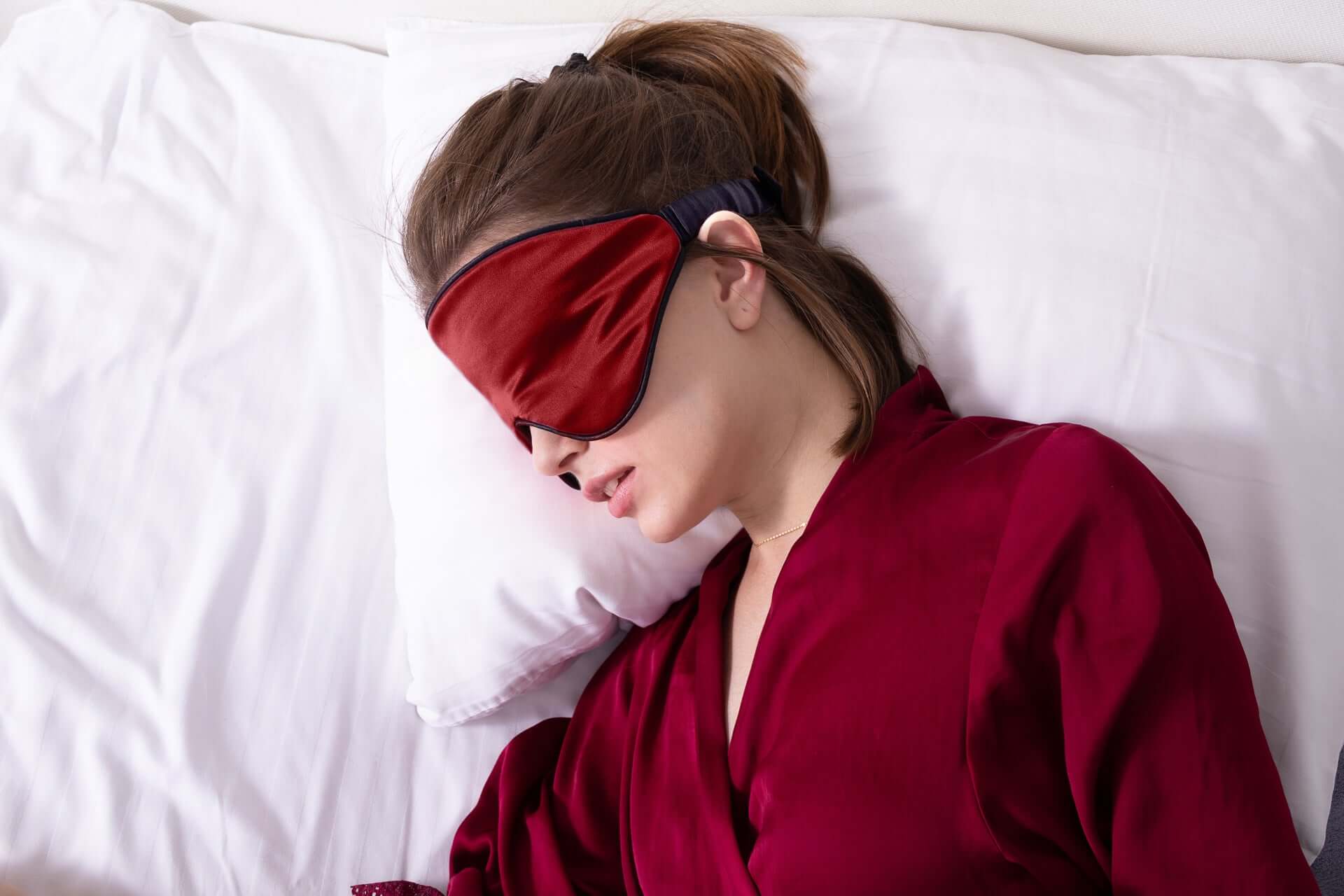 Woman wearing a Quietstore 3.0 non-slip silk sleep mask, promoting restful sleep in a cozy, elegant setting.