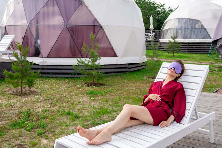 Woman relaxing outdoors in a silk sleep mask near unique dome structures, showcasing comfort and serenity.