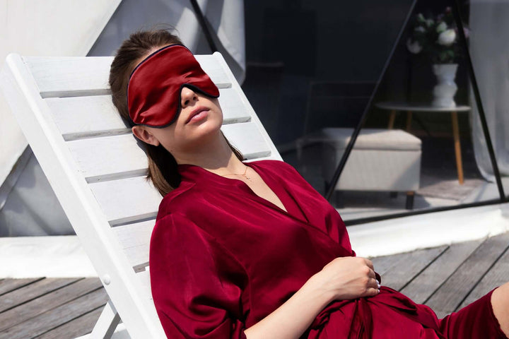Woman wearing a luxurious silk sleep mask relaxing on a lounge chair, promoting restful sleep and comfort.