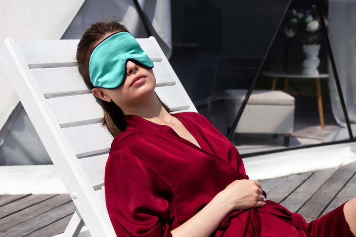 Woman relaxing in a silk sleep mask on a lounge chair, showcasing the Quietstore 3.0 non-slip strap design.