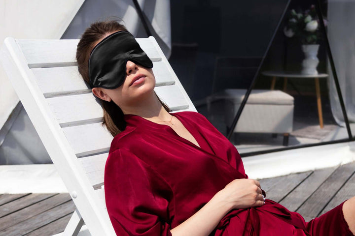 Woman relaxing in a silk sleep mask, wearing a velvet robe, enjoying peaceful rest outdoors.