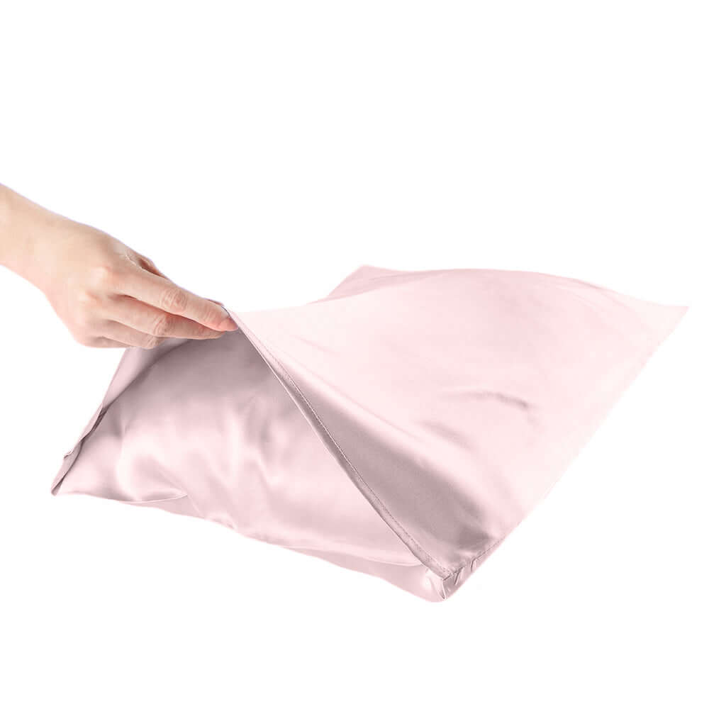 Hand holding a silky pink pillowcase, showcasing its smooth texture for hair and skin care.