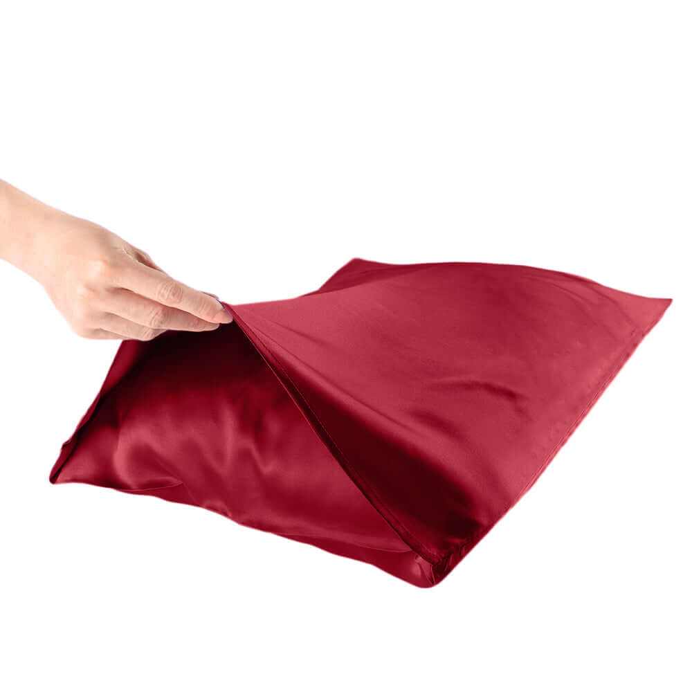 Hand holding a deep red silk pillowcase, showcasing its smooth texture and luxurious fabric.