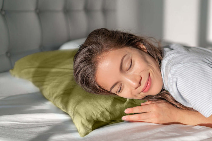 Woman peacefully resting on a green silk pillowcase, highlighting hair and skin benefits.