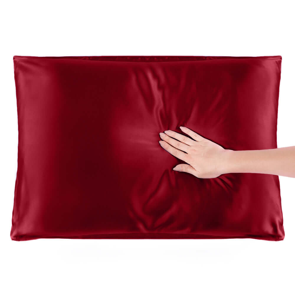 Hand gently pressing a luxurious red silk pillowcase, showcasing its smooth texture and quality.