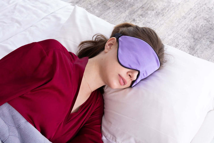 Woman sleeping with a purple silk sleep mask, promoting comfort and restful sleep, on a cozy bed.