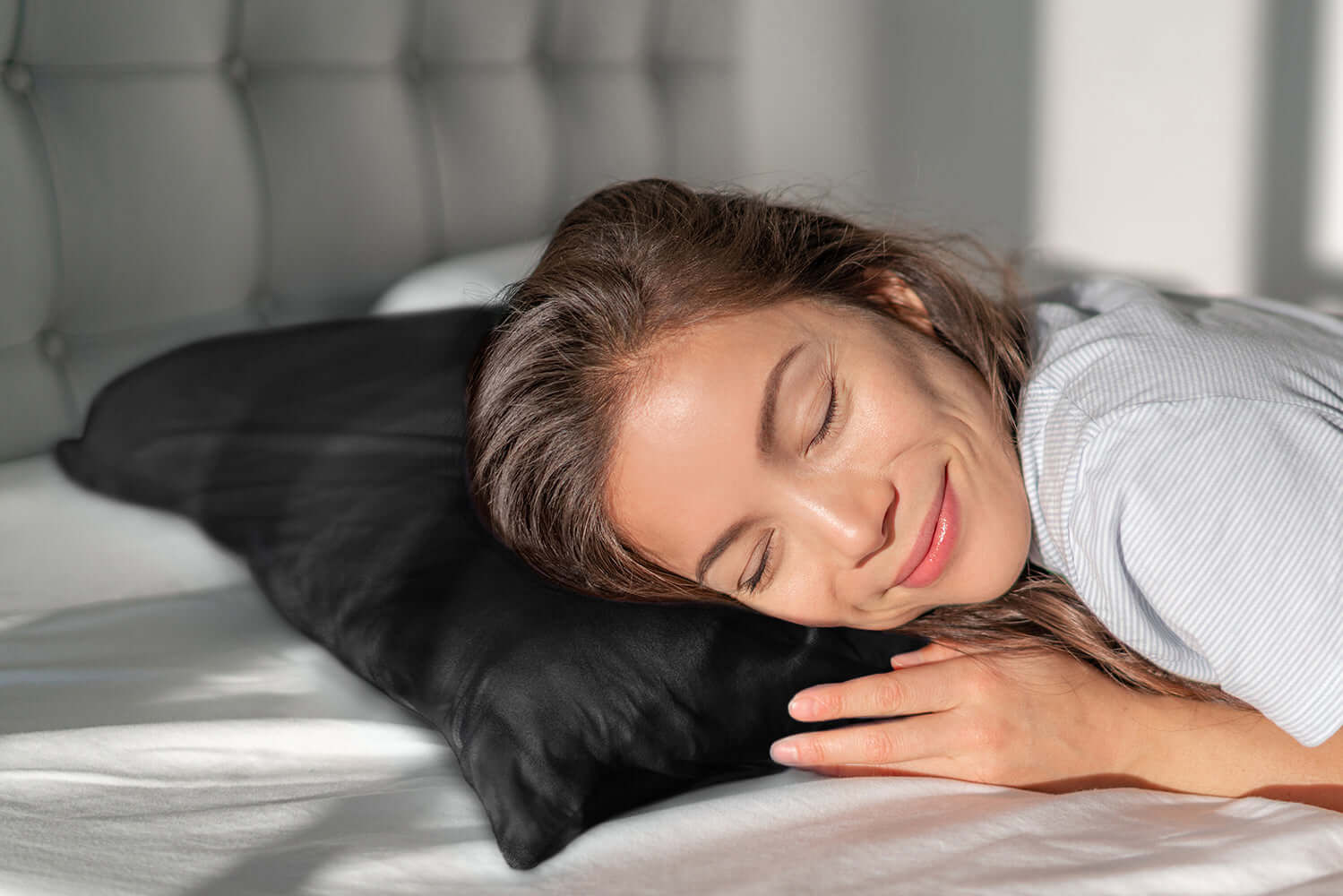 Woman resting on a black silk pillowcase, promoting healthy hair and skin.