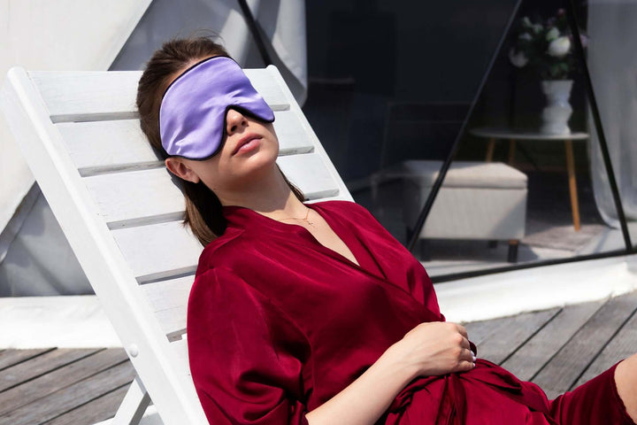 Woman relaxing in a silk sleep mask on a lounge chair, promoting restful sleep and luxury comfort.