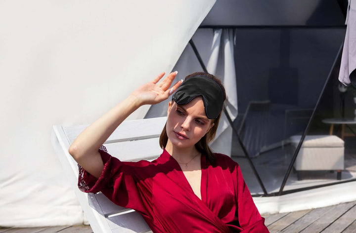 Woman relaxing with Quietstore 3.0 silk sleep mask, showcasing comfort and secure fit in a stylish setting.