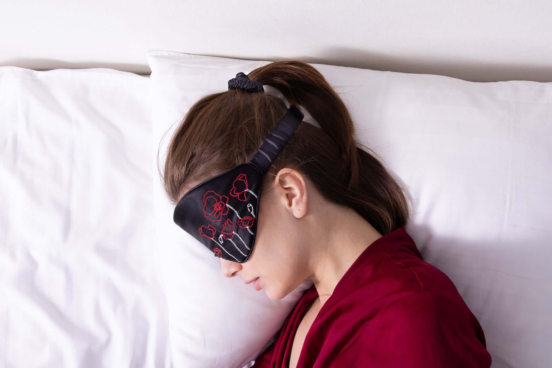 Woman wearing Quietstore 3.1 Silk Sleep Mask with Ukrainian embroidery while resting on a white pillow.