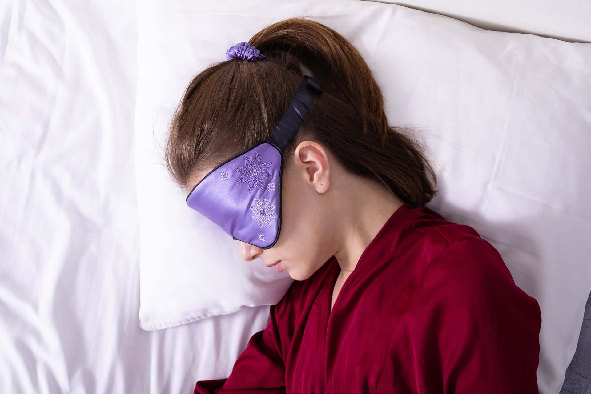 Young girl wearing a Quietstore Silk Sleep Mask with Ukrainian embroidery while resting on a pillow.