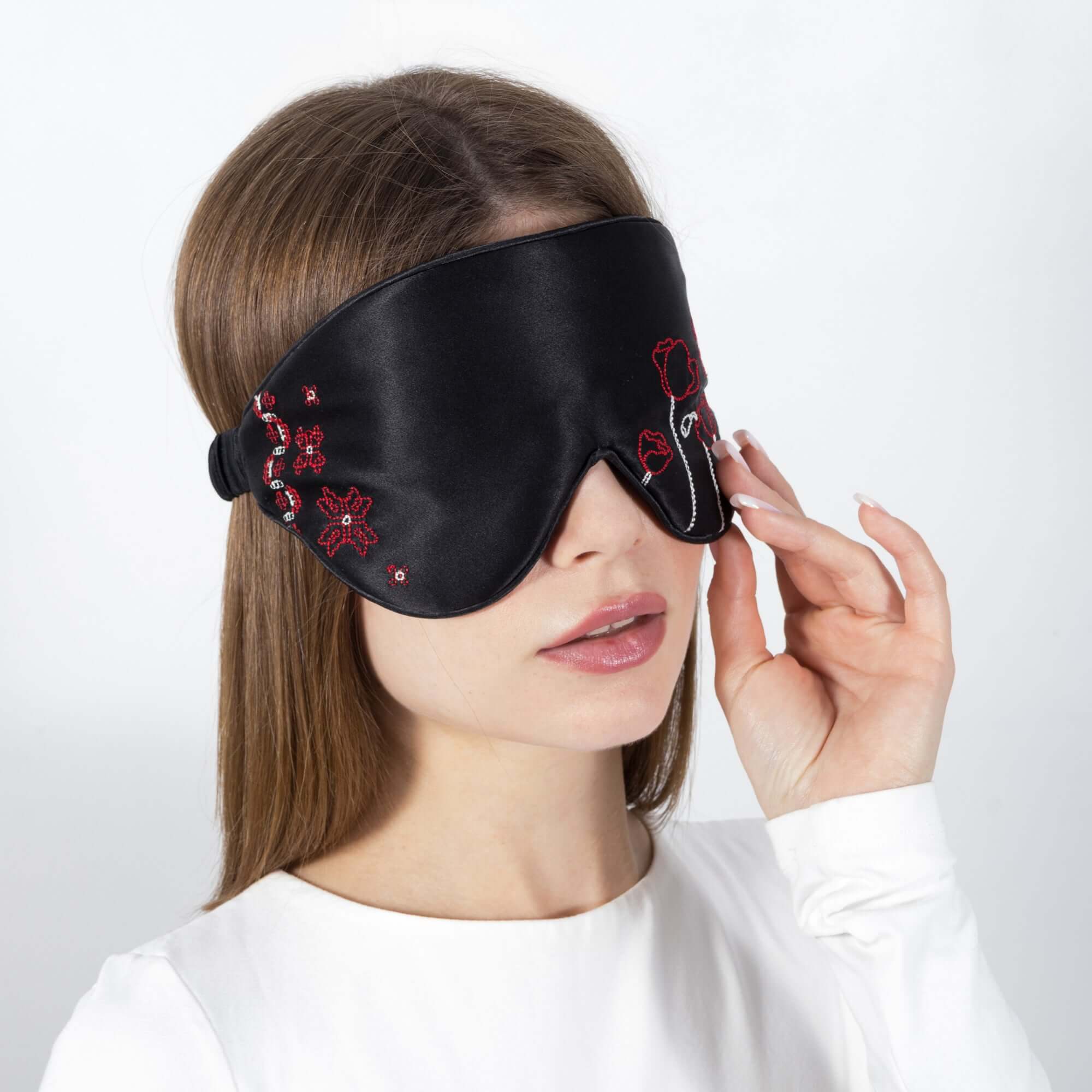 Woman adjusting Quietstore silk sleep mask with Ukrainian embroidery, showcasing its smooth texture and design.