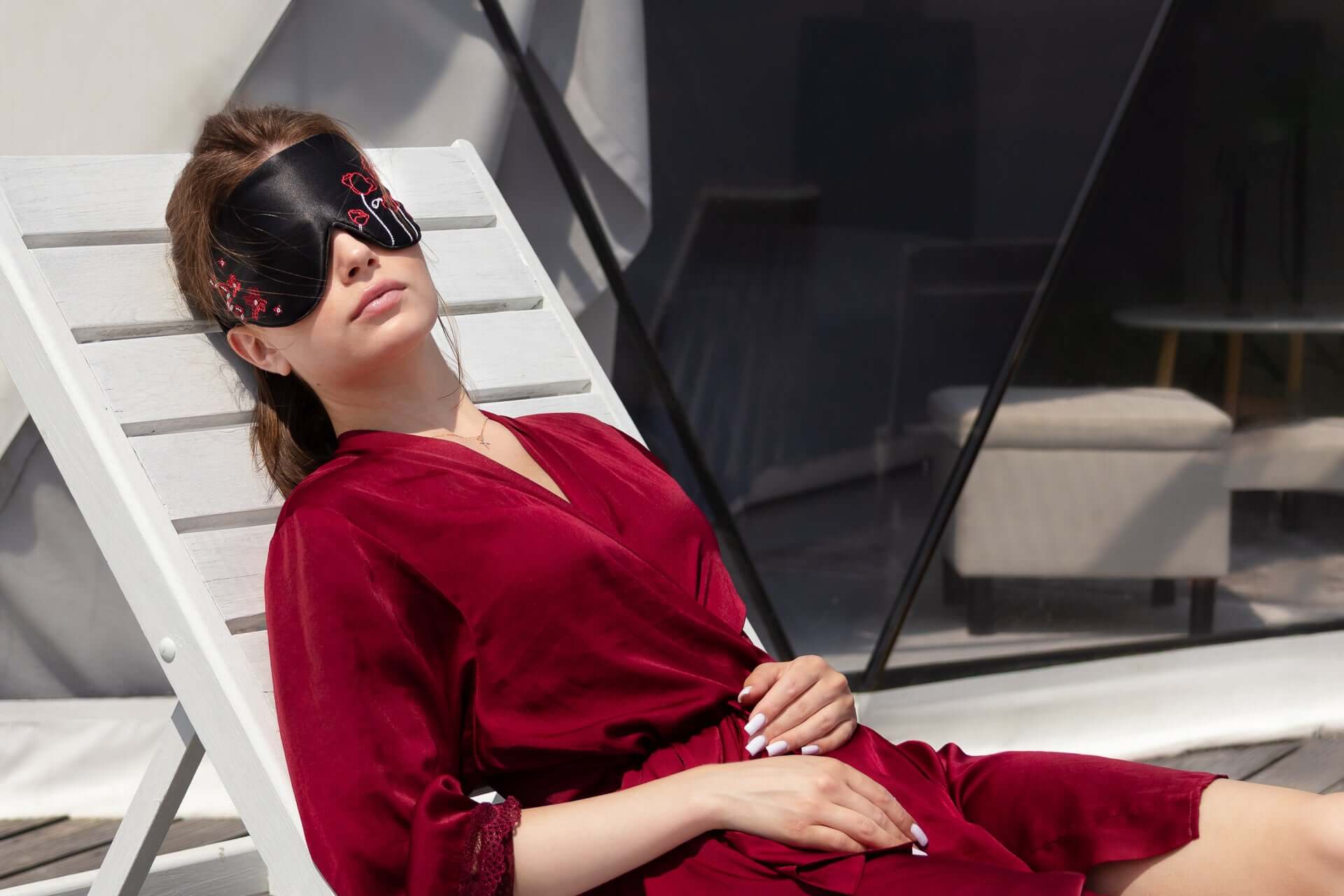 Woman relaxing wearing Quietstore 3.1 silk sleep mask with Ukrainian embroidery, in a stylish red robe.