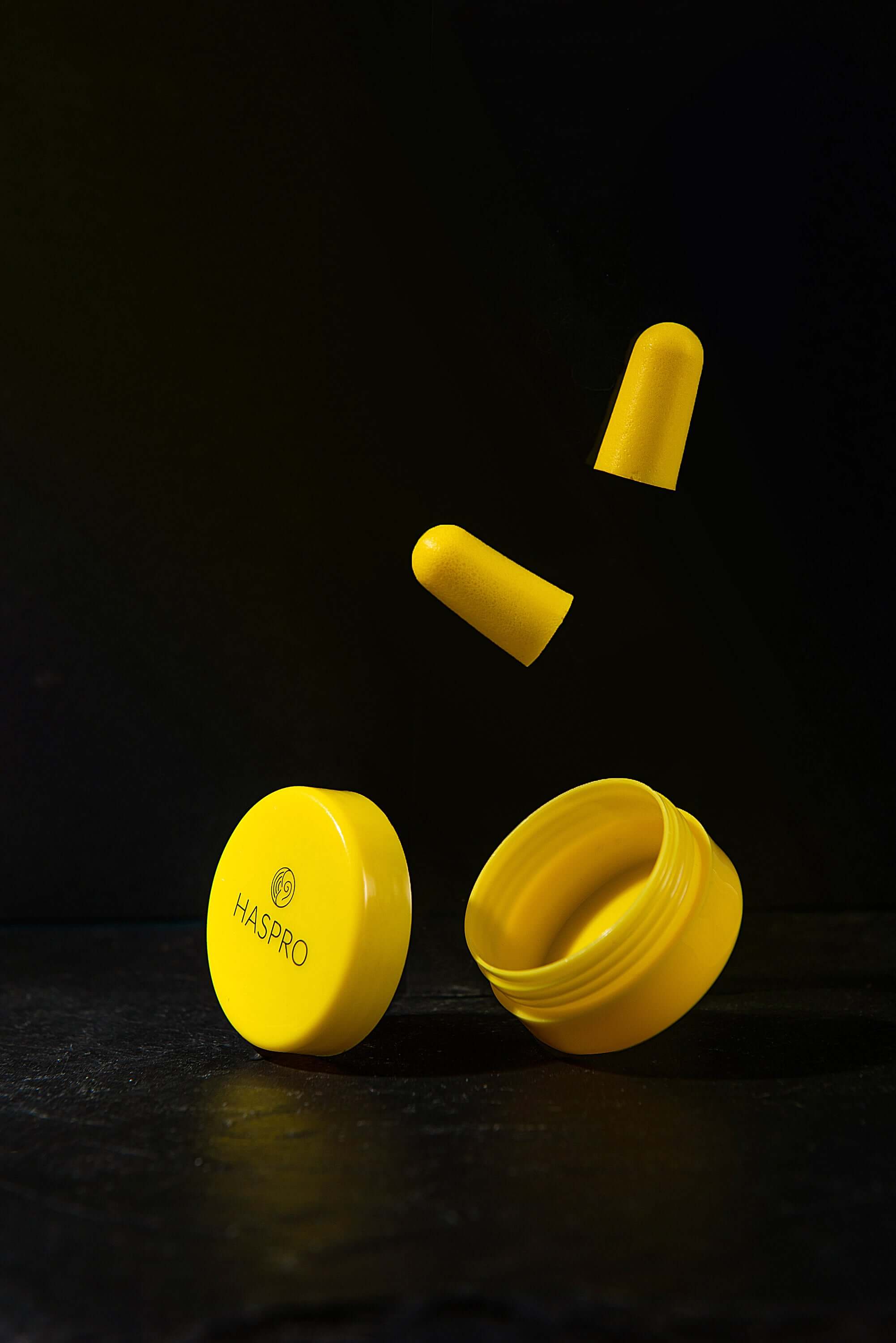Yellow HASPRO earplug container with foam earplugs floating above, highlighting noise reduction and portability.